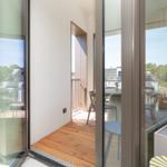 Durchgehende Glasfront öffnet sich zu einer Terrasse mit Holzboden und Gartenblick.