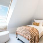 Ein Schlafzimmer mit Dachschrägen, Bett, Sessel und Fenster.
