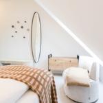 Schlafzimmer mit Bett, Sessel und Spiegel an schräger Wand.