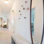 Flur mit Hocker, Wandhalterungen und Blick in Wohn- und Badezimmer.