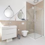 Badezimmer mit Dusche, Waschbecken und Toilette. Zwei runde Spiegel an der Wand.