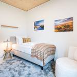 Schlafzimmer mit Bett, Sessel und Wandbildern.