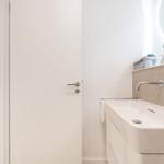 Badezimmer mit Waschbecken, Spiegel und Tür zum Ankleideraum.