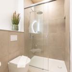 Badezimmer mit Dusche, Toilette und Waschbecken. Weiße Fliesen und Pflanze.