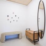 Ein Raum mit Bank, Schrank und Wandspiegel. An der Wand hängt eine runde Kunstinstallation.