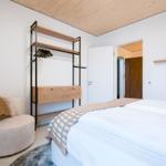 Schlafzimmer mit Bett, Kleiderschrank und Sessel. Holzdecke und weiße Wände.