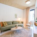 Ein Wohnzimmer mit grünem Sofa, Holzboden und großem Fenster.