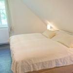 Schlafzimmer mit Bett, zwei Nachttischen und Lampen. Dachschräge und floral gemustertes Bettzeug.