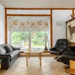 Living room with leather sofa, two chairs, and large window overlooking garden.