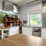 Kitchen with white cabinets, stainless steel hood, and wooden table. Window shows green trees.