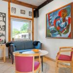 Living area with sofa, two chairs, and wall art. View of garden through window.
