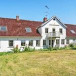 White holiday home with red roof and balcony. Surrounded by greenery with garden.