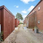 Gehweg zwischen roten Holzcontainern und Backsteinhaus mit Fenstern.