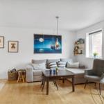 Wohnzimmer mit Sofa, Sitzgelegenheit und Wandbild. Holzboden und Fenster.