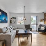 Wohnzimmer mit Sofa, Tisch und Fernseher an Holzwand. Tür führt auf Balkon.