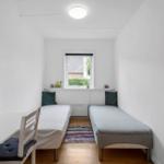 Zwei Einzelbetten stehen im Raum. Fenster, Teppich und Stuhl sind sichtbar.
