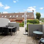 Terrasse mit Tisch, Stühlen und Sonnenschirm. Hinterhof mit Zaun und Blick auf Haus.