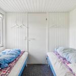 Zwei Betten mit blauen Decken und gemusterten Laken stehen in einem Raum mit weißen Wänden und einem Fenster.