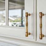 Weißer Schrank mit messingfarbenen Griffen und Glasfronten.