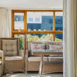 Wohnbereich mit Rattanmöbeln, Glas-Tisch und großem Fenster mit Blick auf Grünflächen.