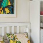 Schlafzimmer mit Bett, Kissen und Wandbild. Neben dem Bett steht ein weißer Schrank.