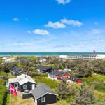 Meerblick mit Strand, Dünen und Häusern unter blauem Himmel mit weißen Wolken.