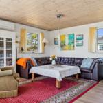 Wohnzimmer mit braunem Ledersofa, rotem Teppich und Holzboden. Fenster mit gelben Vorhängen.