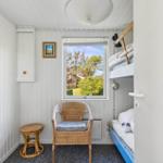 Kleines Schlafzimmer mit Schlafcouch, Stuhl und Fensterblick auf Grün.