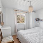 Bedroom with white bed, window, wardrobe, and chair. Ceiling and walls are white paneled.