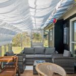 Terrace with seating, sun sail, and wooden tray. View of green garden.