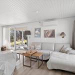 Living room with sofa, coffee table, and wooden floor. Windows and door to garden. Fireplace and wall art.