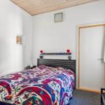 Schlafzimmer mit Bett, Kopfteil und Wandspiegel. Decke aus Holz.