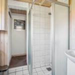 Badezimmer mit Dusche, Waschbecken und Toilette. Holzwände und Fliesenboden.