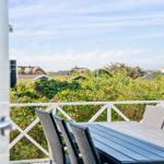 Terrasse mit Tisch und Stühlen, Blick auf grüne Hecke und Häuser im Hintergrund.