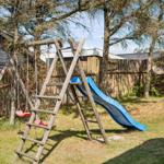 Hinterhof mit Holzspielplatz, Rutsche und Schaukel unter Bäumen.