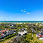 Strandnahe Häuser mit Dünengrund und blauem Meer im Hintergrund.