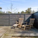 Terrace with two wooden loungers and dark wood railing. Background: trees and clear sky.