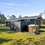 A house with wooden cladding and an outdoor tub. Surrounded by grass and trees.