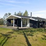 Modern wooden cabin with terrace, grill, and garden. Surrounded by trees and grass.