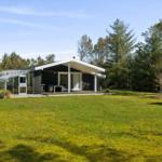 Modern cabin with terrace and garden. Surrounded by trees under blue sky.