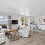 Living and dining area with sofa, dining table, and TV. Wooden floor and white walls.