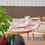 Wooden table with placemats, mugs, plates, and basket of bread.