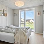 Bedroom with bed, window, and wooden floor. Walls with vertical panels.