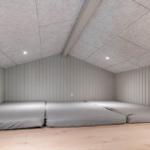 Room with two mattresses on wooden floor and vertically paneled walls.
