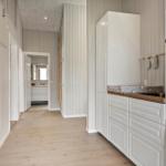 Laundry room with washer and dryer, white cabinets, and wooden floor. Hallway leads to the bathroom.