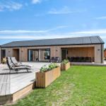 Modern wooden house with terrace, loungers, and garden. Adjacent building with hot tub.