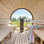 Wood sauna with round window, benches, and wood stove. View of grassland and building.