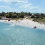 Beach with white sand, turquoise water, and some people. A red rescue boat is on the shore.