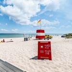 Beach with sand, sea, and red lighthouse. Sun and weather information visible.