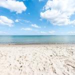 View of the beach with sand and calm sea under blue sky with white clouds.
